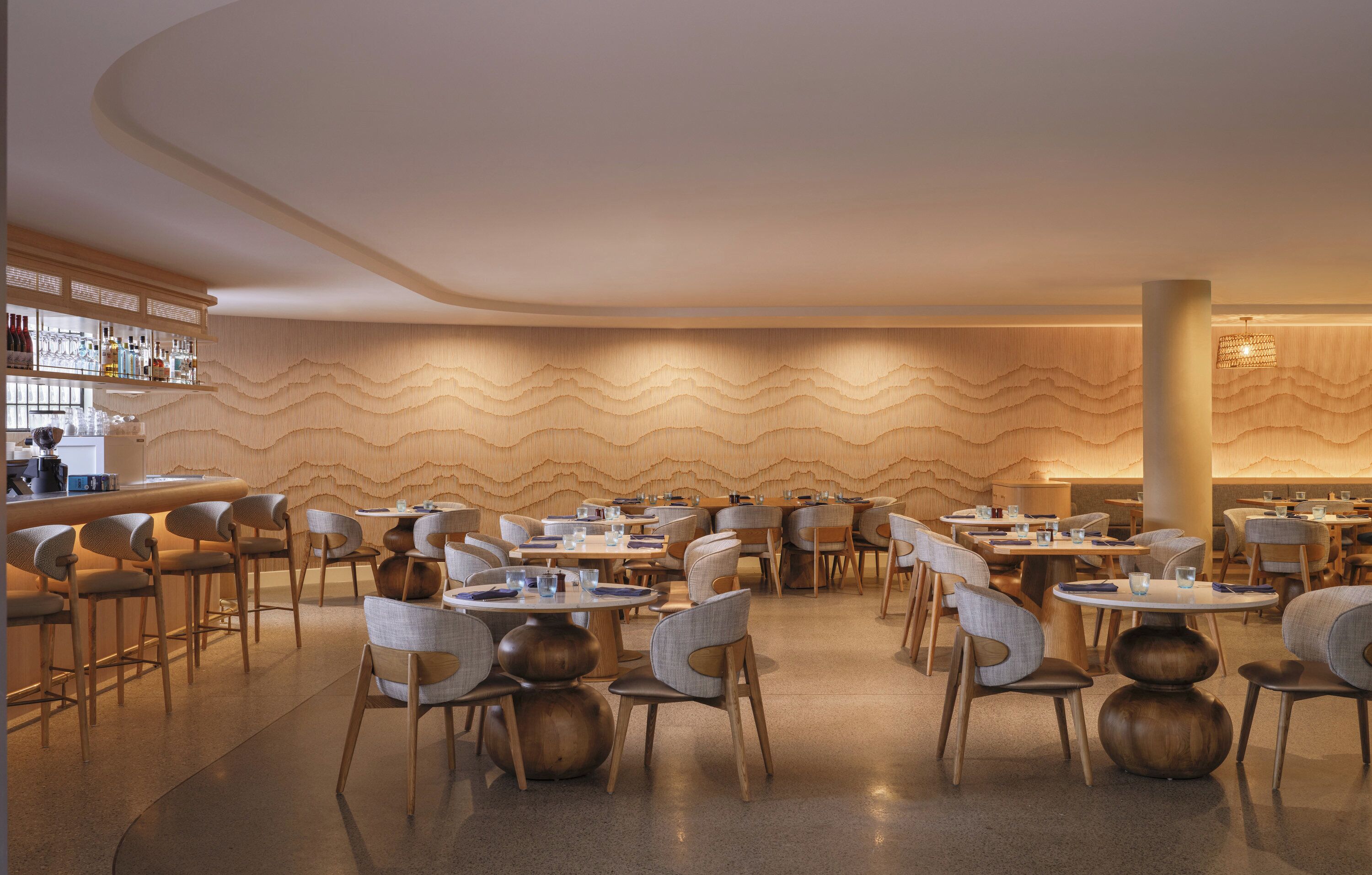 Un restaurante moderno con mesas y sillas redondas, una zona de bar y un diseño de pared ondulado único.