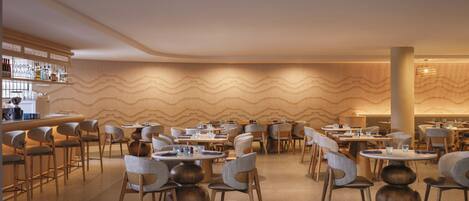 Un restaurante moderno con mesas y sillas redondas, una zona de bar y un diseño de pared ondulado único.