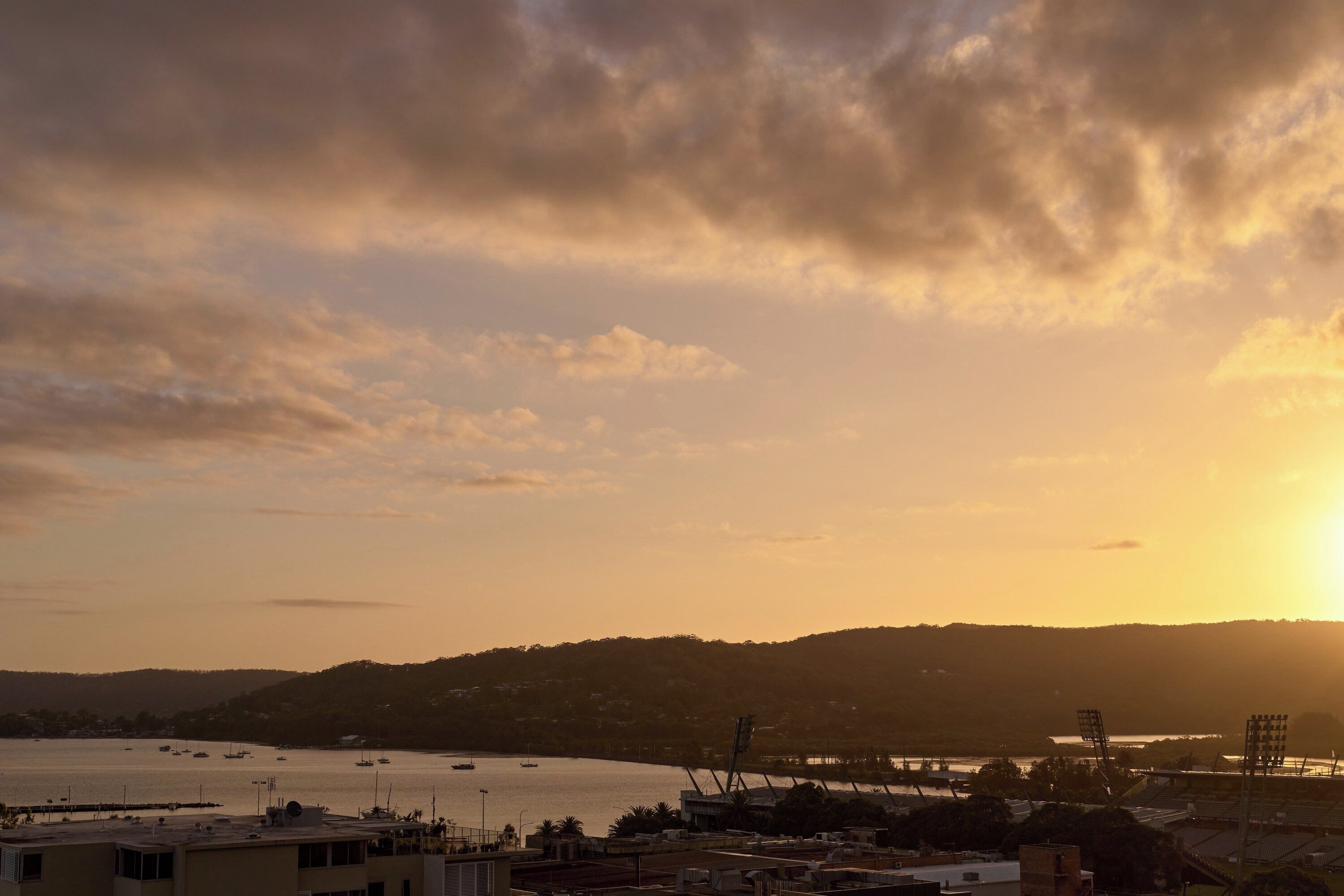 A coastal view with boats, a stadium, and buildings during sunset.