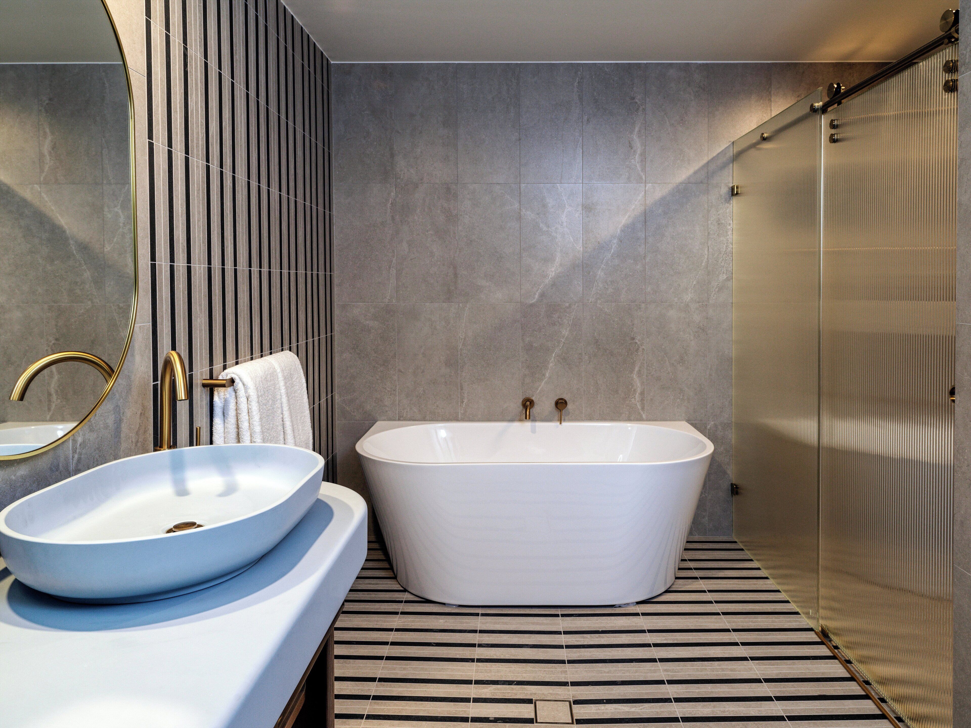 Un baño moderno con una bañera independiente, un lavamanos sobre encimera y un espejo grande.