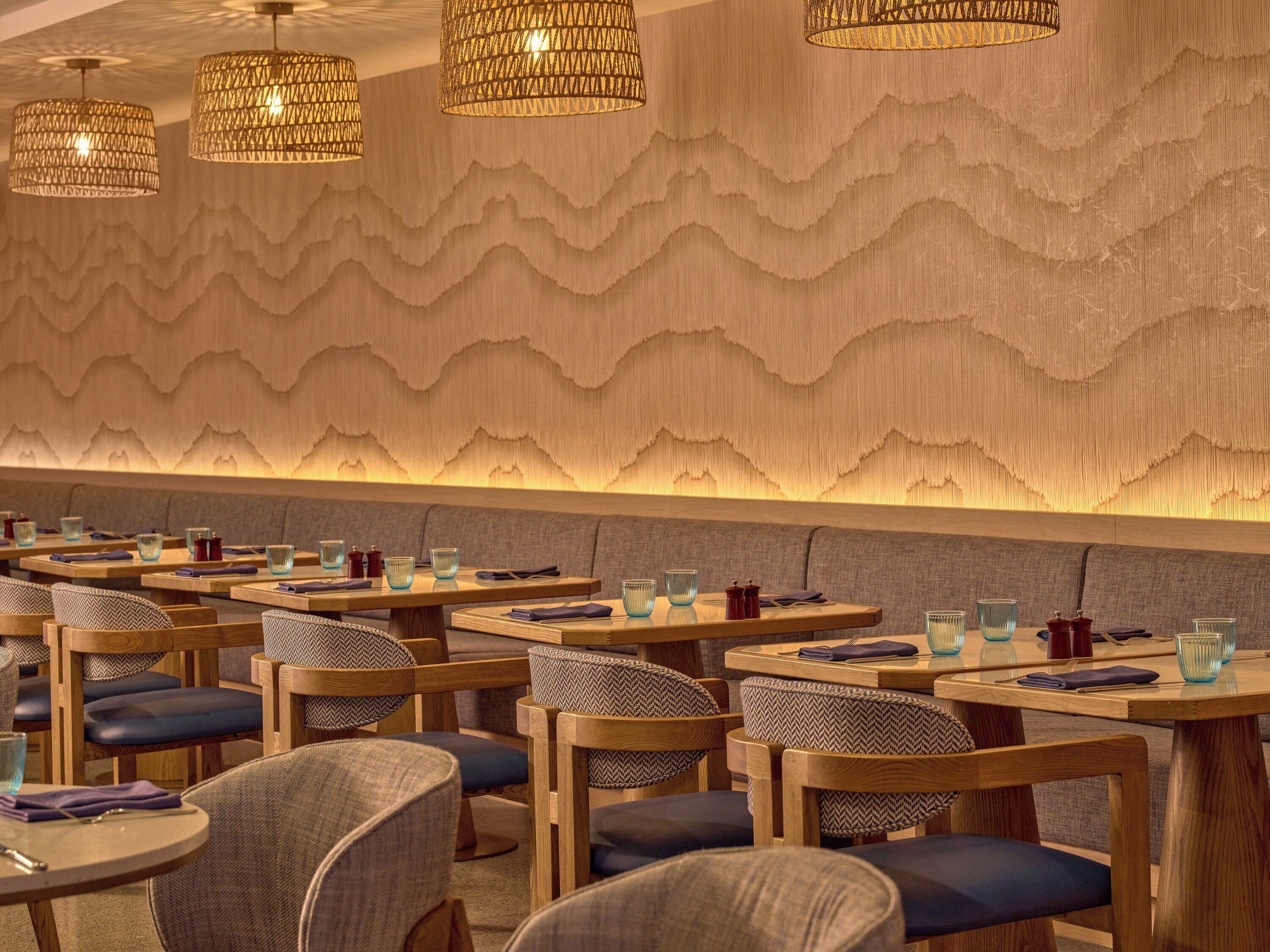 A restaurant with wooden tables and chairs, a patterned wall, and hanging lamps.