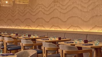 Un restaurante con mesas y sillas de madera, un muro decorado y lámparas colgantes.