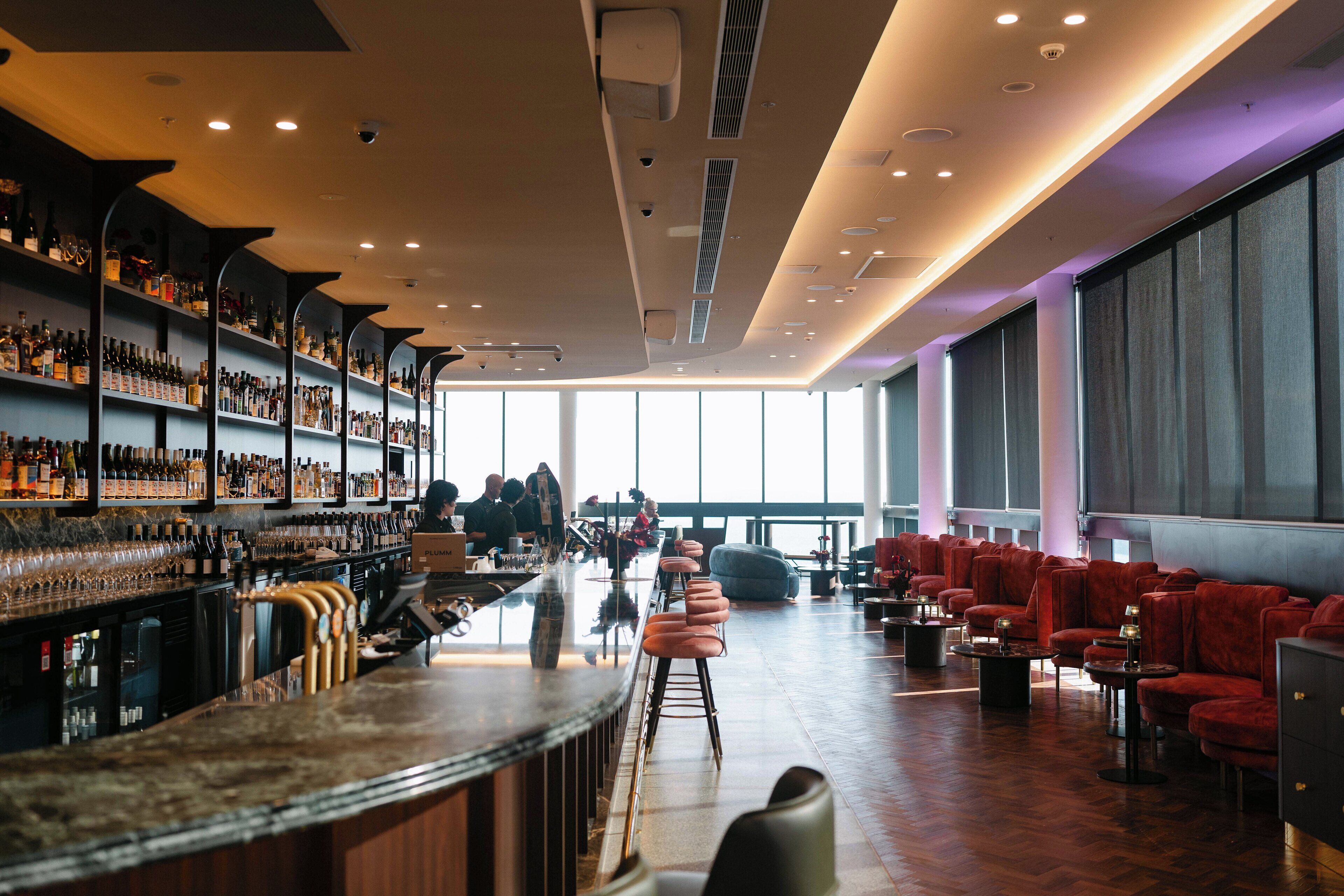 A bar area with shelves of bottles, bar stools, and a seating area with red chairs.