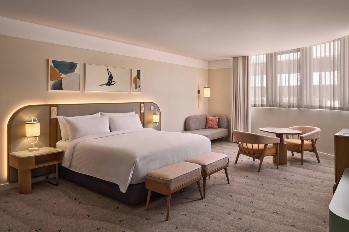 A hotel room with a large bed, bedside tables, a seating area with a sofa and chairs, and artwork on the walls.