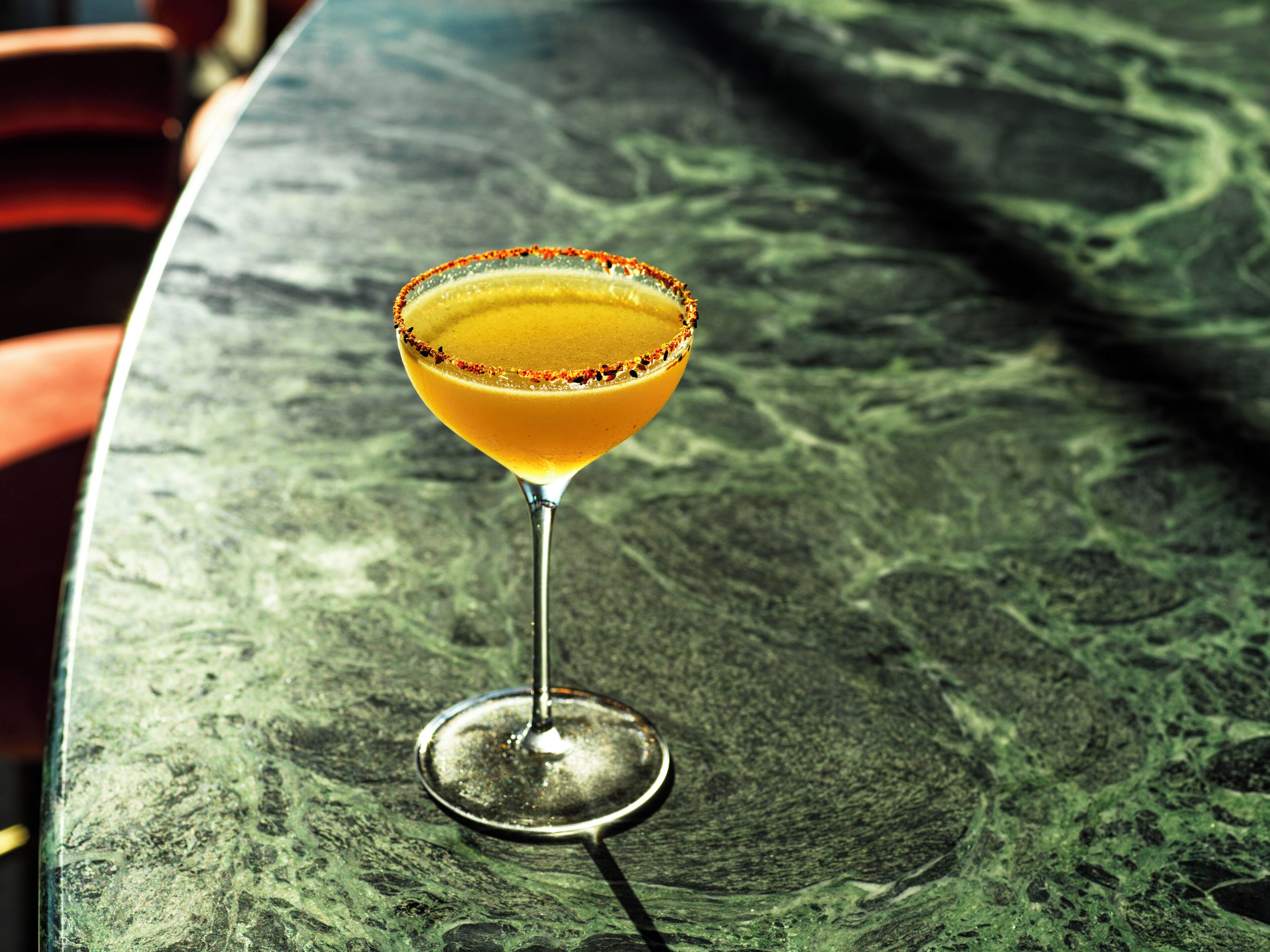 A margarita cocktail in a martini glass with a salted rim, placed on a green marble table.