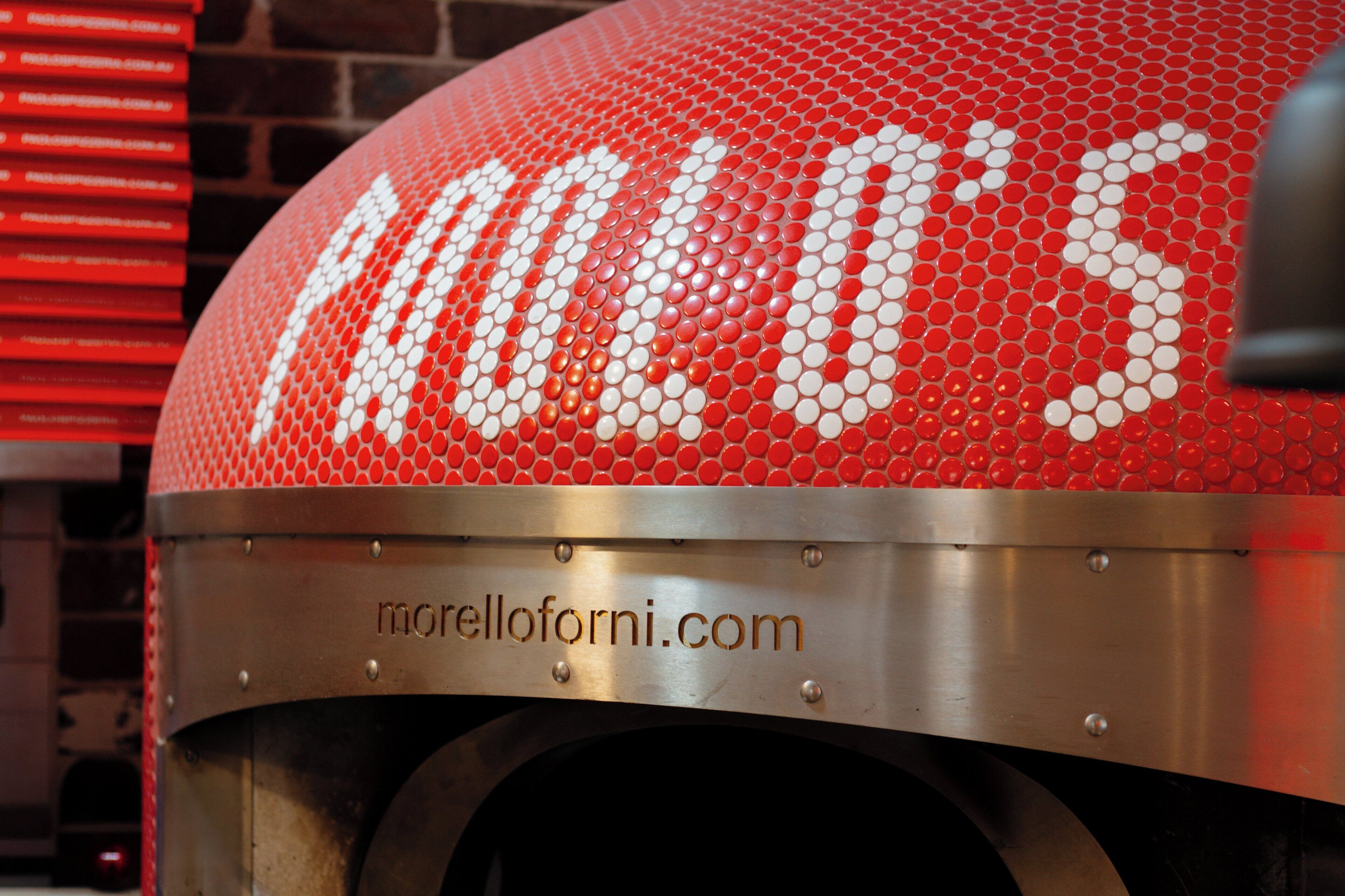 Un four à pizza orné d’une mosaïque rouge et blanche, avec l’inscription « morelloforni.com ».