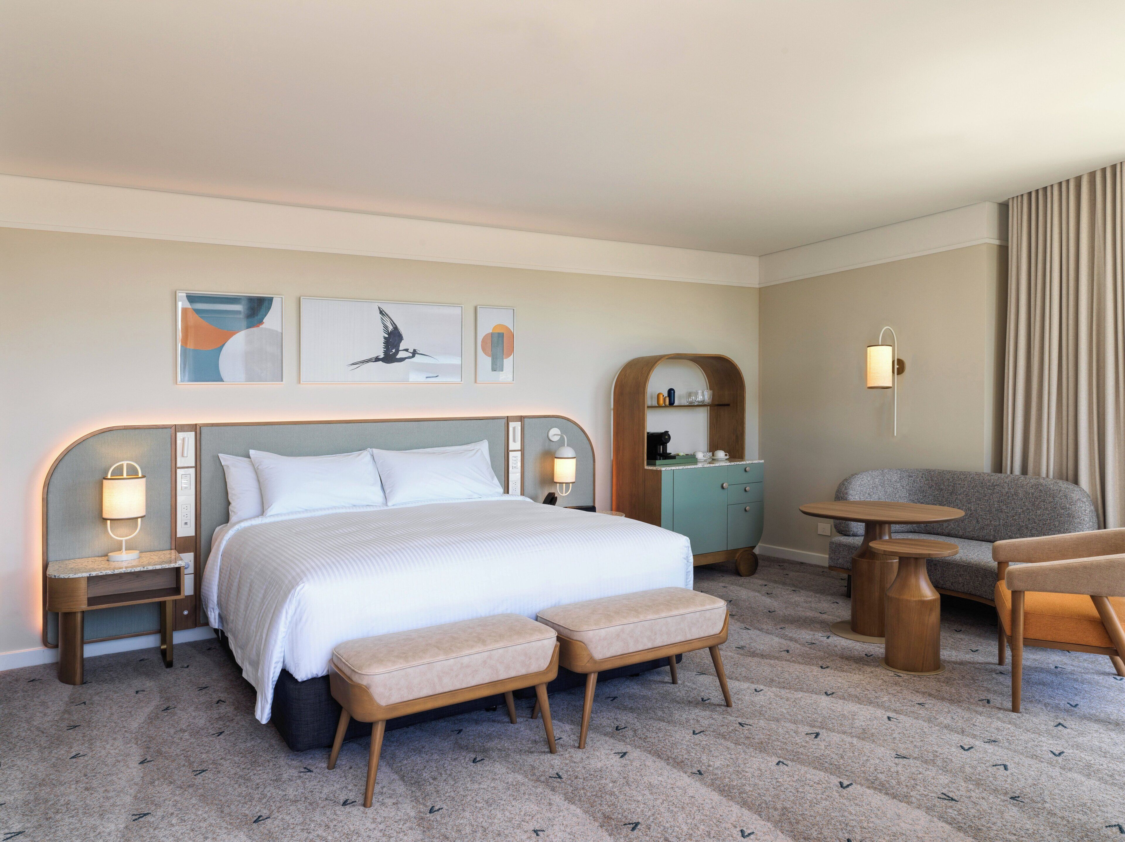A hotel room with a bed, two bedside tables, a bench, a sofa, a small table, and a wall-mounted shelf.