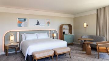 A hotel room with a bed, two bedside tables, a bench, a sofa, a small table, and a wall-mounted shelf.