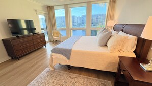 A hotel room with a large bed, a TV on a wooden dresser, a chair, and a view of buildings through the windows. - Beach place in Longboat Key. (Longboat Key)