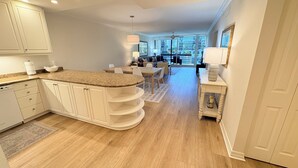 A modern kitchen with white cabinetry, a granite countertop, and a dining area with a table and chairs. - Beach place in Longboat Key. (Longboat Key)