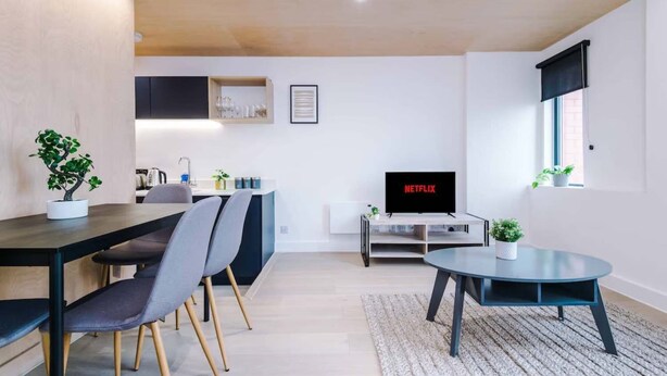 Una sala de estar moderna con comedor, televisor y cocina al fondo.