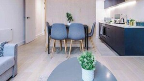 Una cocina moderna con armarios oscuros, una zona de comedor con una mesa redonda y sillas, y una pequeña planta en maceta en el suelo.