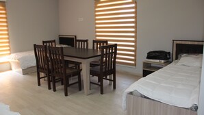 A room with a bed, a desk, and chairs. There is a window with blinds, a bedside table, and a TV. - Hostel Asham (Gusar)