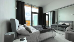 A modern hotel room with a large bed, a bedside table, a mirror, and a view of the city through the window. - Modern Luxury in Manchester (Manchester)