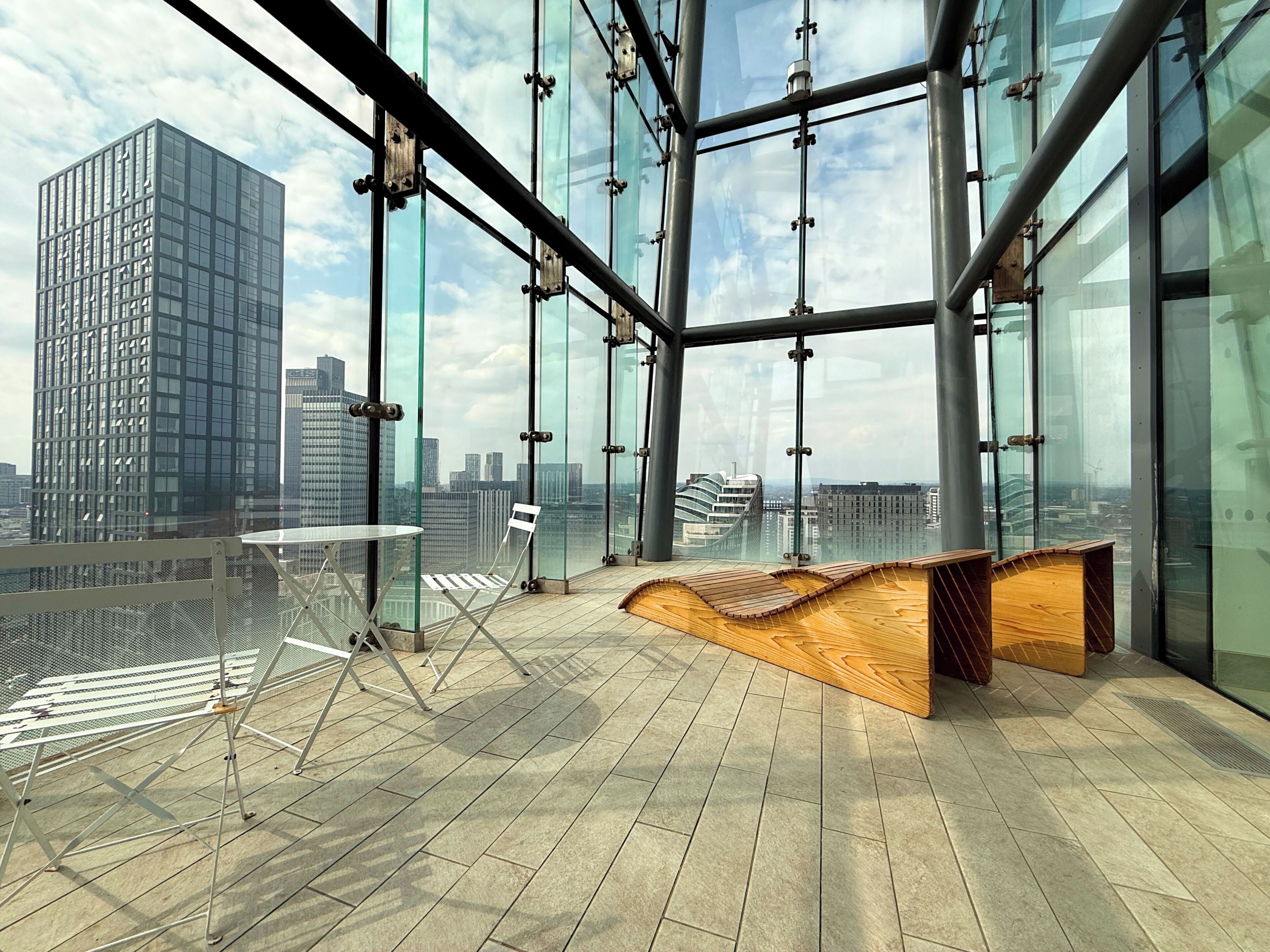Un interior moderno con vistas panorámicas de la ciudad, un banco de madera y una mesa plegable de metal.