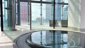 A modern indoor pool area with a glass enclosure, a circular pool, and a view of surrounding buildings.