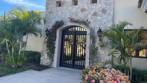 Un edificio de piedra con una reja negra, rodeado de plantas y flores tropicales.
