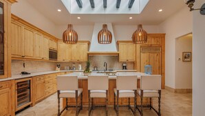 Una cocina moderna con armarios de madera, una isla central con taburetes de bar, iluminación colgante y un tragaluz.