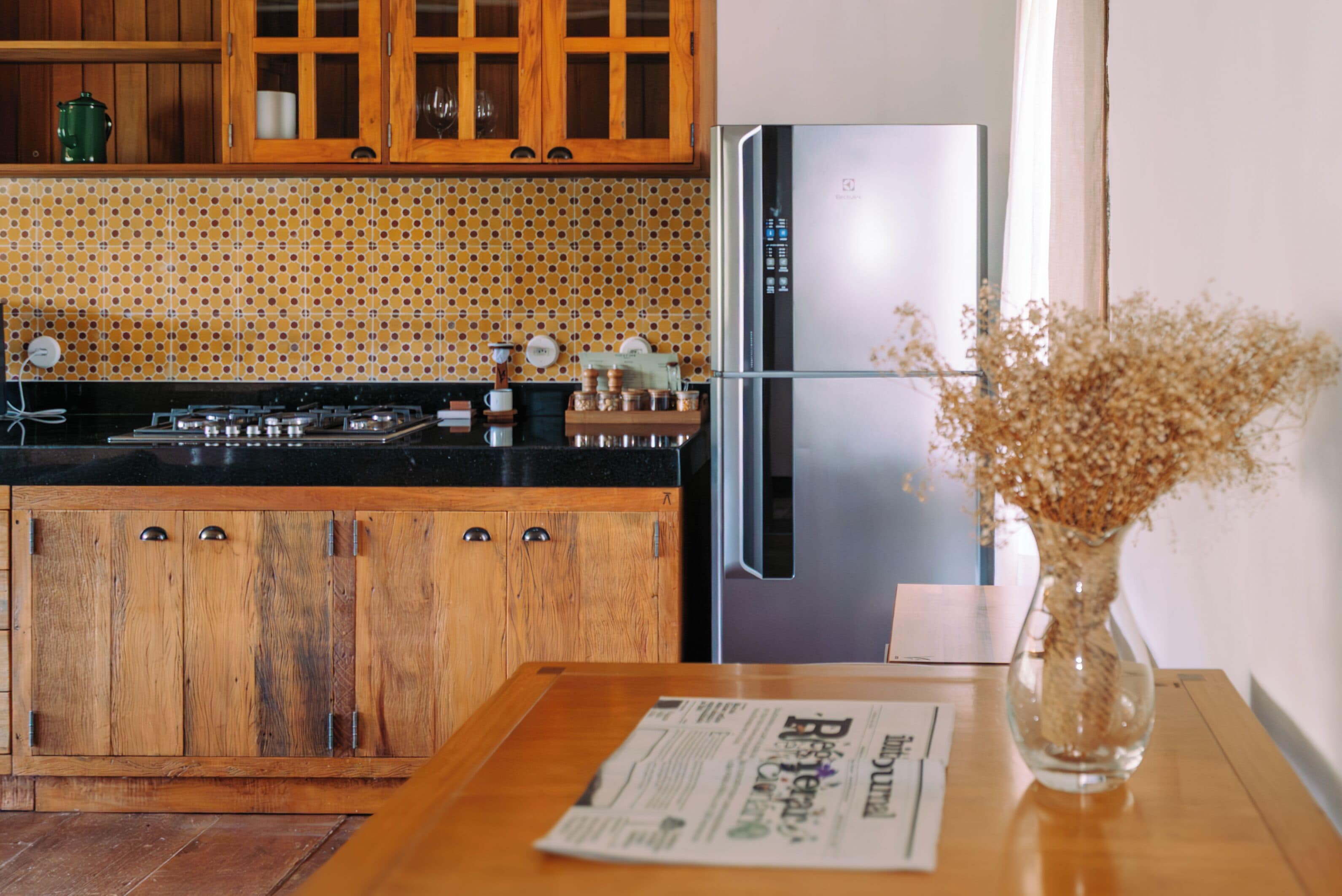 A kitchen with wooden cabinets, a stainless steel refrigerator, and a vase with dried flowers on the table.