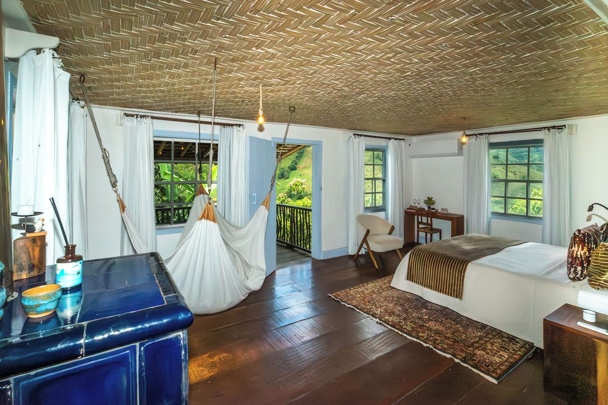 A room with a bed, a desk, a chair, a hanging chair, and a view of greenery outside.