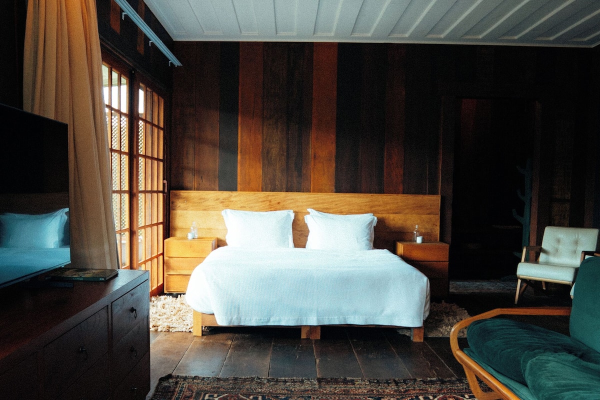 A bedroom with a large bed, wooden headboard, bedside tables, a green sofa, and a patterned rug.