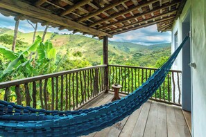 A hammock on a wooden balcony overlooking a lush landscape with hills. - Ibiti Village (Lima Duarte)