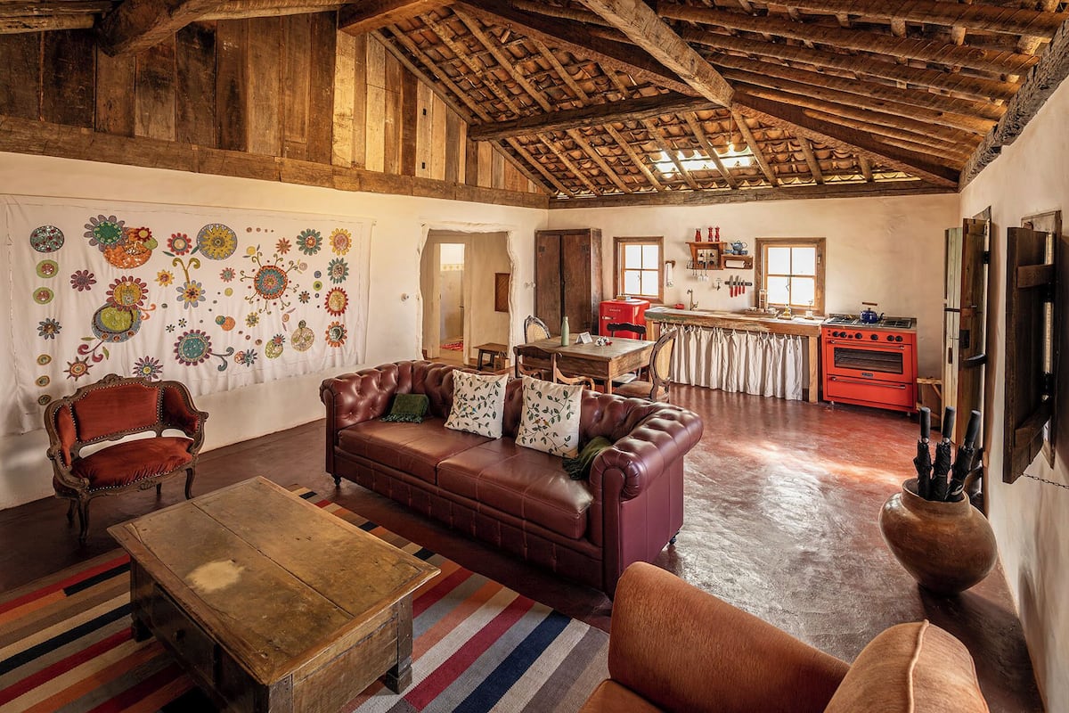 A rustic interior with a leather sofa, wooden coffee table, and a dining area with a red oven.