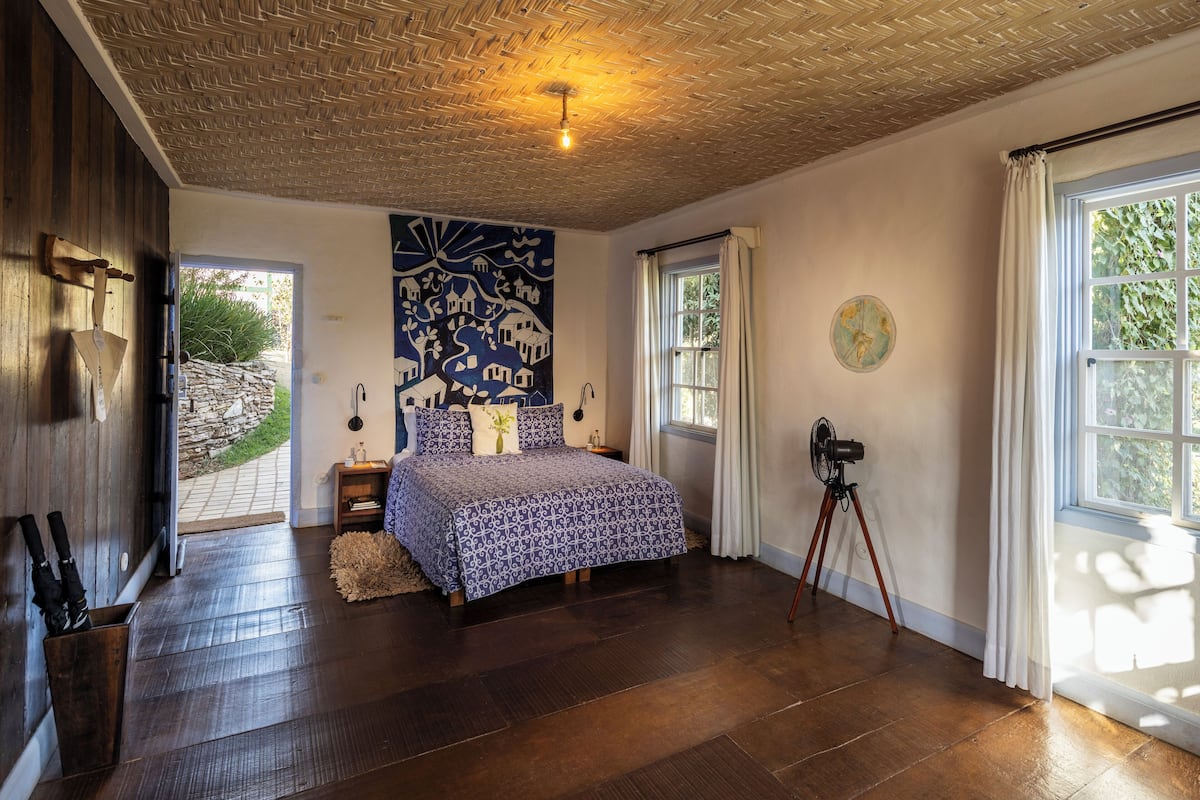 A bedroom with a bed, a map on the wall, a window, and a fan.
