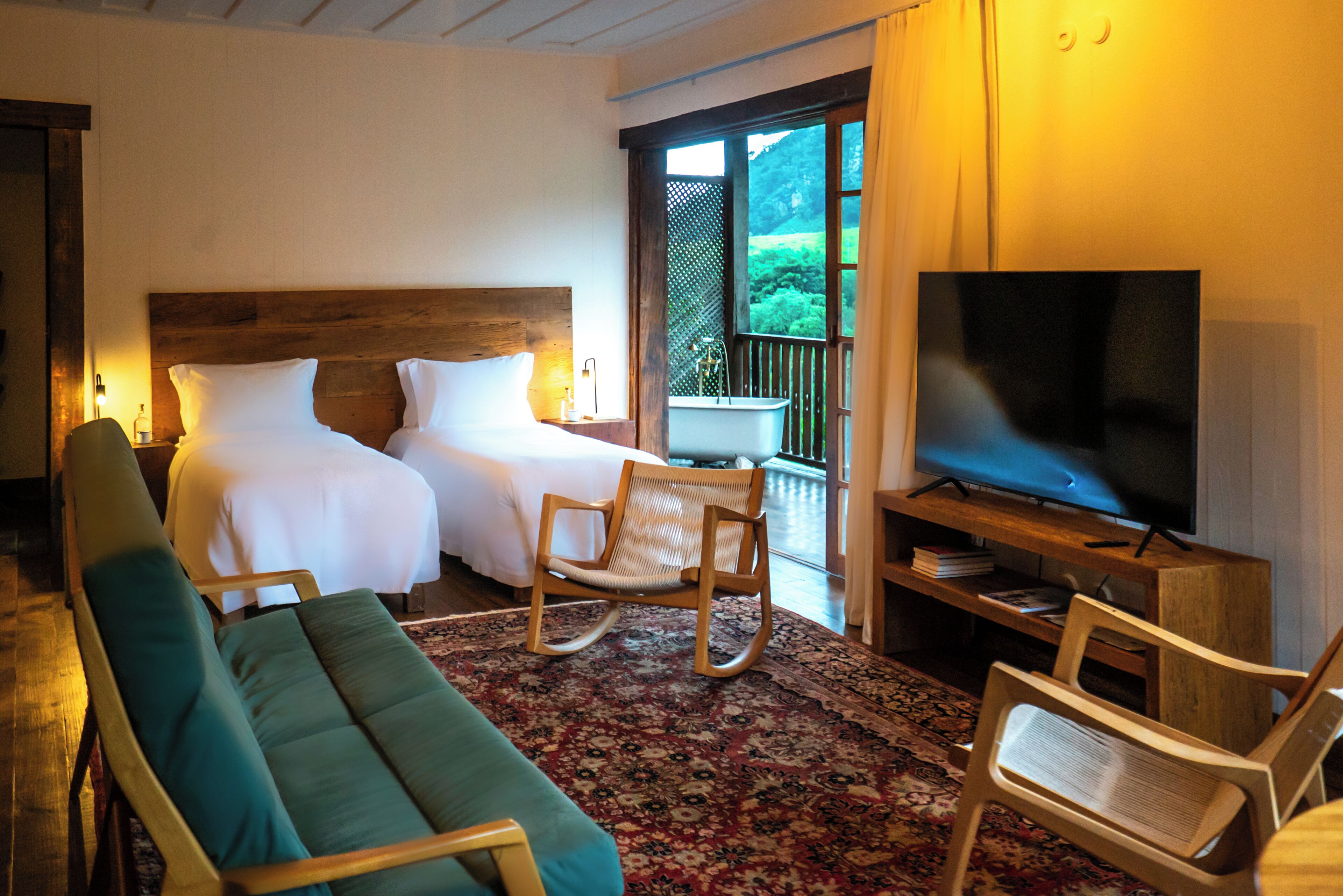 A hotel room with a bed, two rocking chairs, a sofa, a television, and a view of greenery outside.