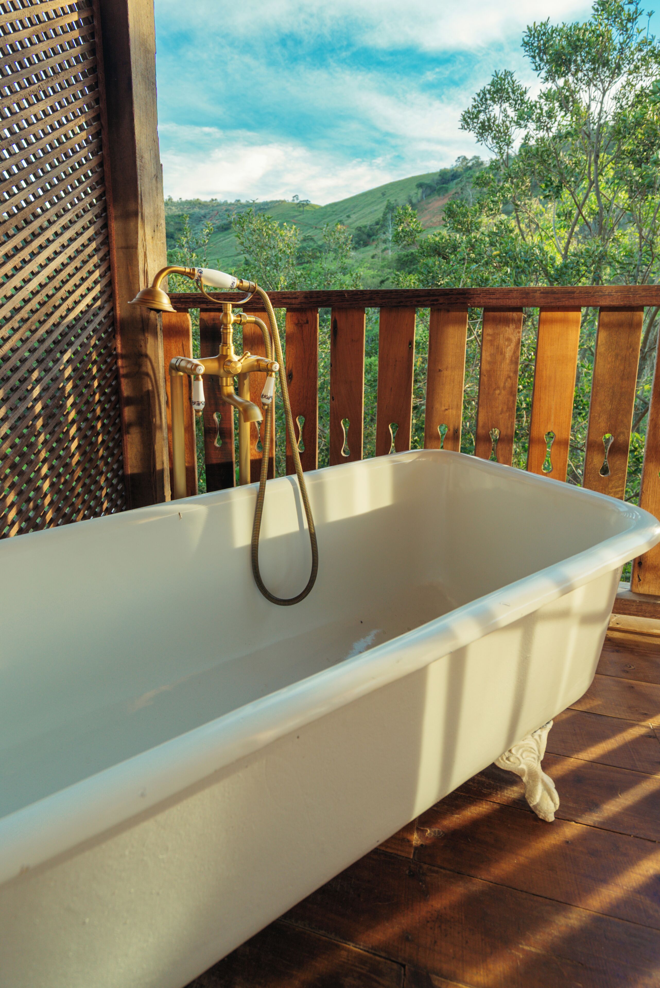 A bathtub with a showerhead on a wooden deck with a view of green hills.
