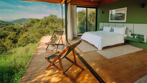 A bedroom with a large bed, a view of the outdoors, and a wooden deck. - Ibiti Village (Lima Duarte)