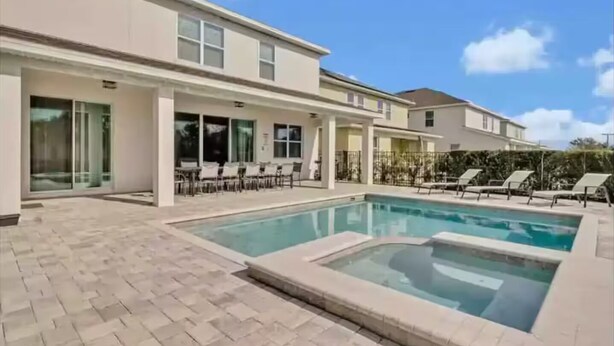 A modern house with a swimming pool, a covered patio with outdoor furniture, and a clear blue sky.