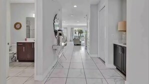 A modern hallway with a kitchen area on the right, featuring cabinets and a countertop.