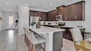 A modern kitchen with dark wood cabinets, a central island with bar stools, stainless steel appliances, and a tiled floor.