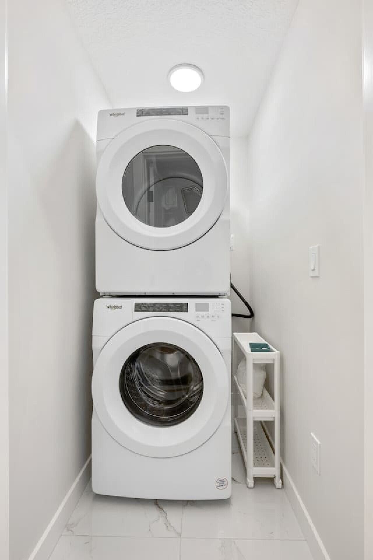 Una sala de lavandería con dos lavadoras Whirlpool apiladas y un estante blanco pequeño.