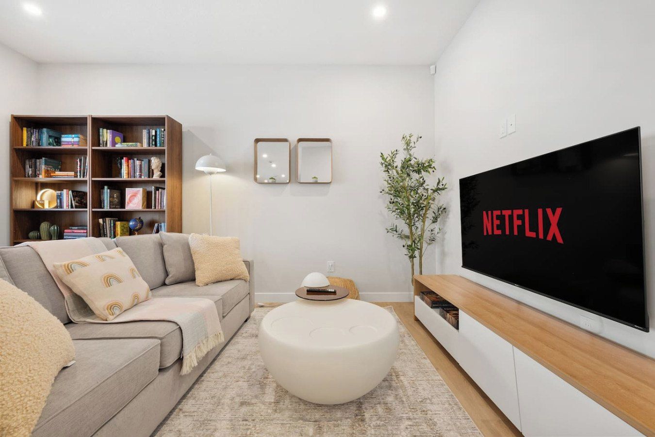 Ein modernes Wohnzimmer mit einer Couch, einem Couchtisch, einem Bücherregal, einem Flachbildfernseher und einer Stehlampe.
