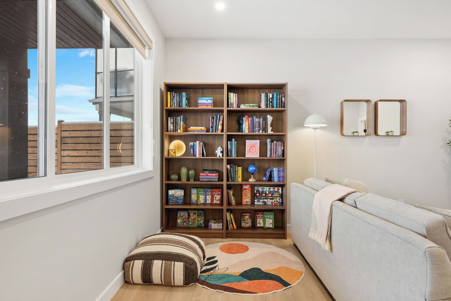 Un salon avec une bibliothèque, un canapé, un tapis rond et une fenêtre.