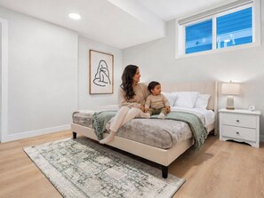 Un dormitorio con cama, mesita de noche, lámpara, un cuadro enmarcado en la pared y ventana con vistas.