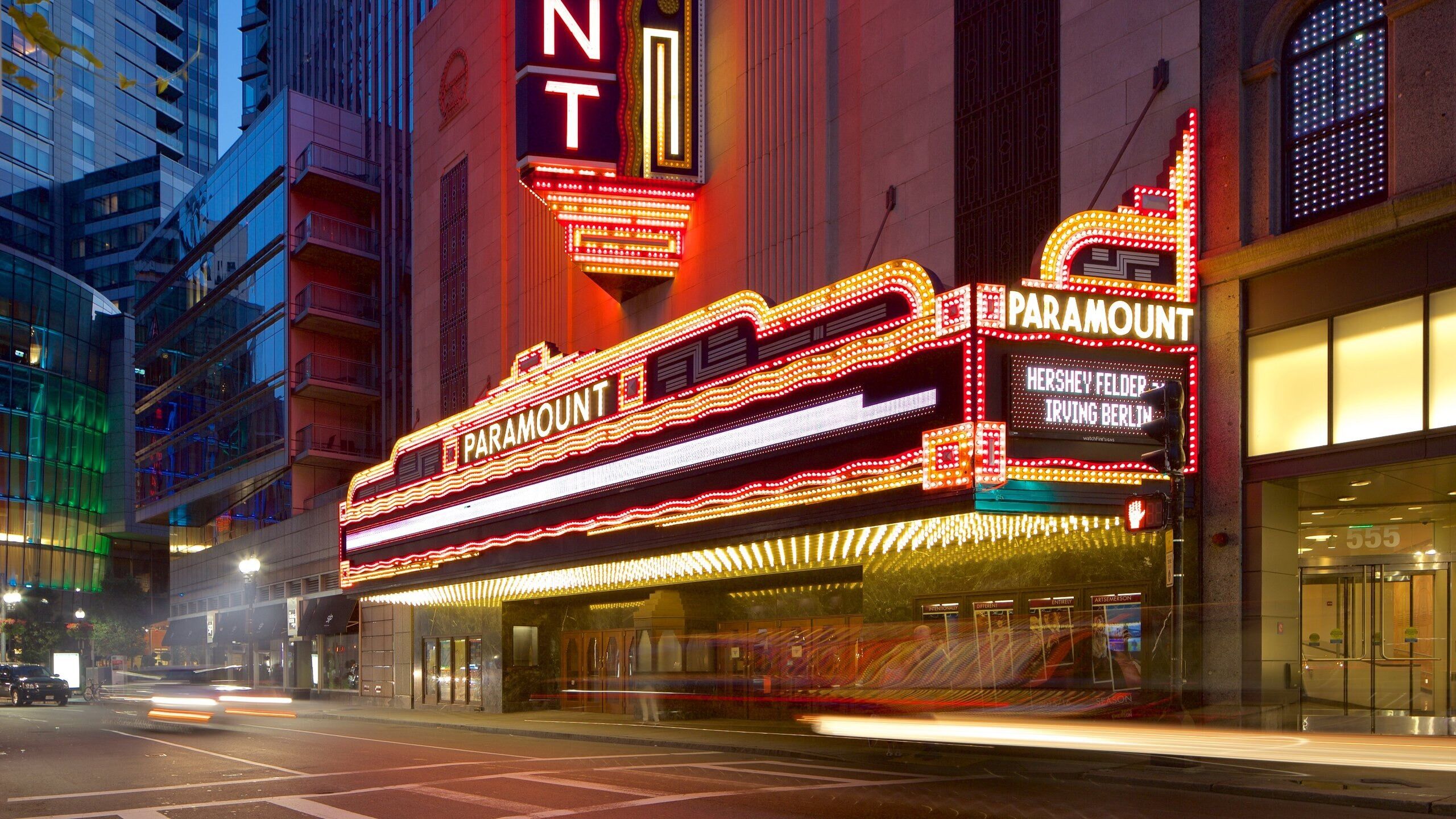 A brightly lit theater with neon signage, including "Paramount" and "Hershey Felder Irving Berlin".