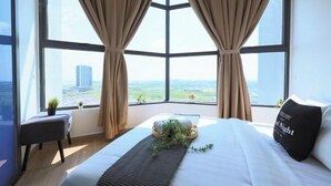 A hotel room with a large window, a bed with a pillow, a small table with a plant, and a view of a cityscape. - Atlantis Residence Premium By I Housing (Melaka)