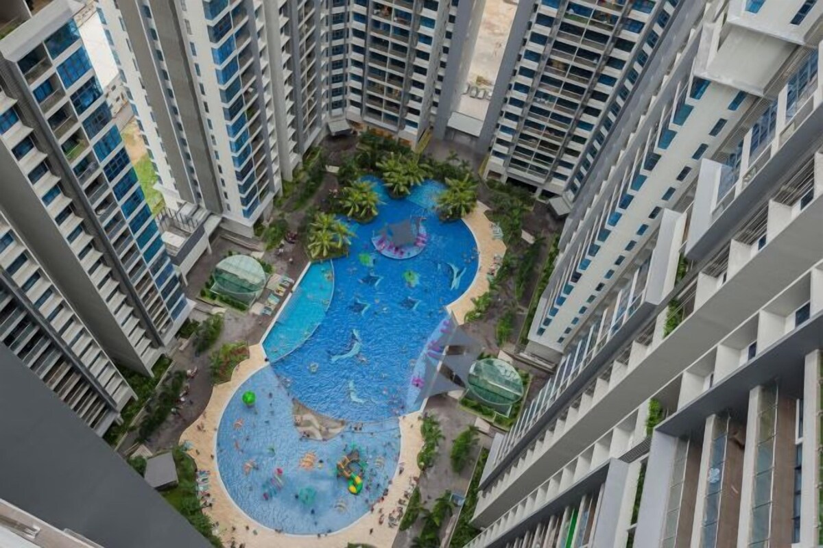 A high-rise building with multiple balconies, a central swimming pool, and surrounding greenery.