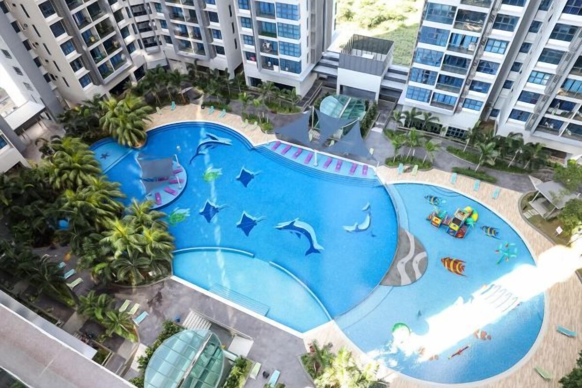 A swimming pool with dolphin-shaped features, surrounded by palm trees and modern buildings.
