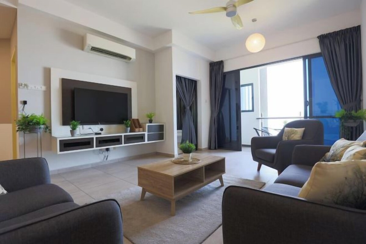 A modern living room with a flat-screen TV, a sofa, a coffee table, and a balcony with curtains.