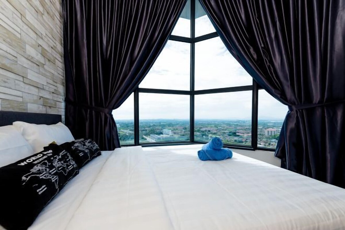 A hotel room with a large bed, a view through a window, and a cityscape.