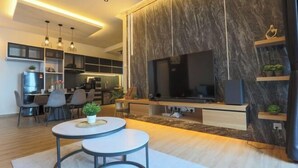 A modern living room with a large TV, built-in shelves, and a dining area with chairs and a table. - Atlantis Residence Premium By I Housing (Melaka)