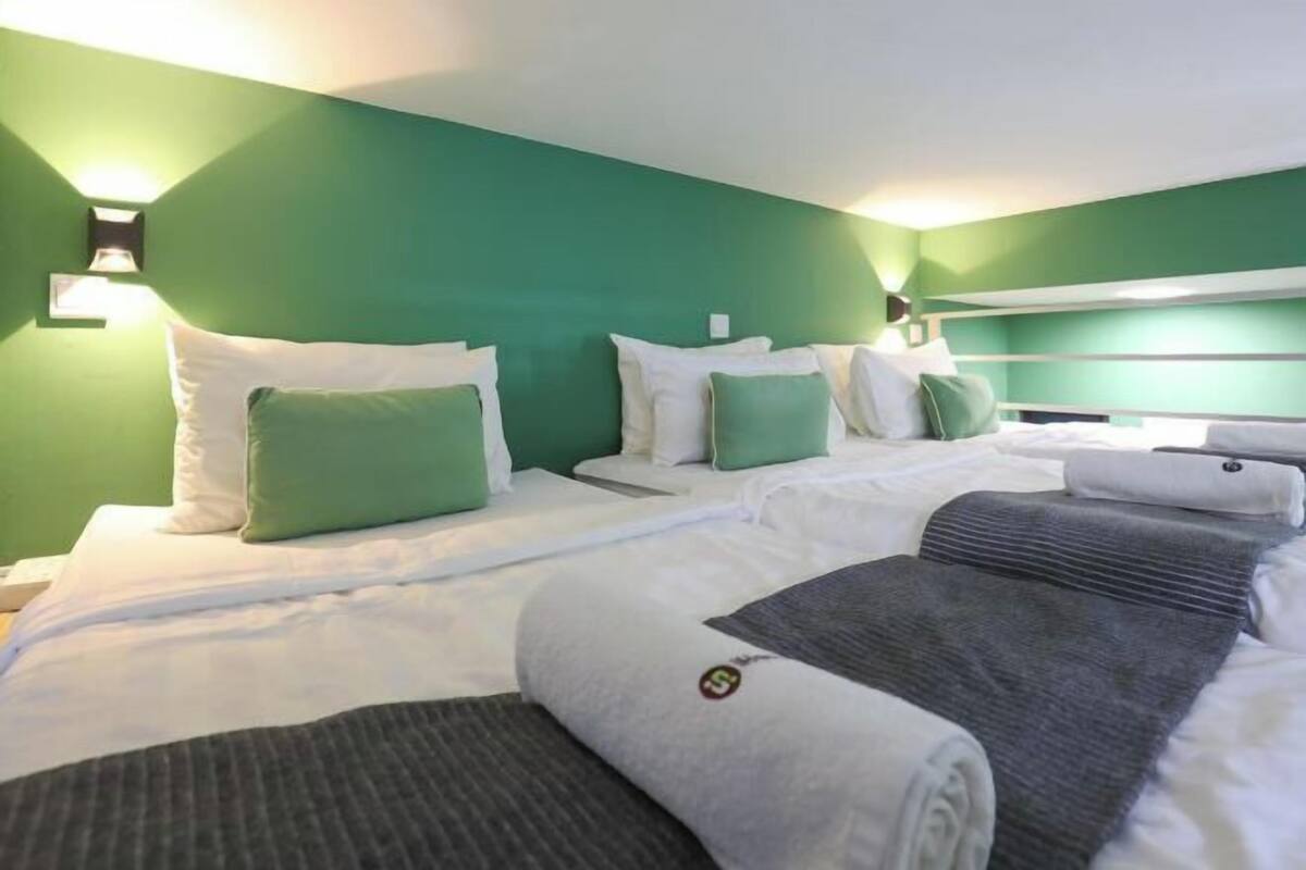 Une chambre d’hôtel avec deux lits, des murs verts, du linge de lit blanc et une tête de lit.