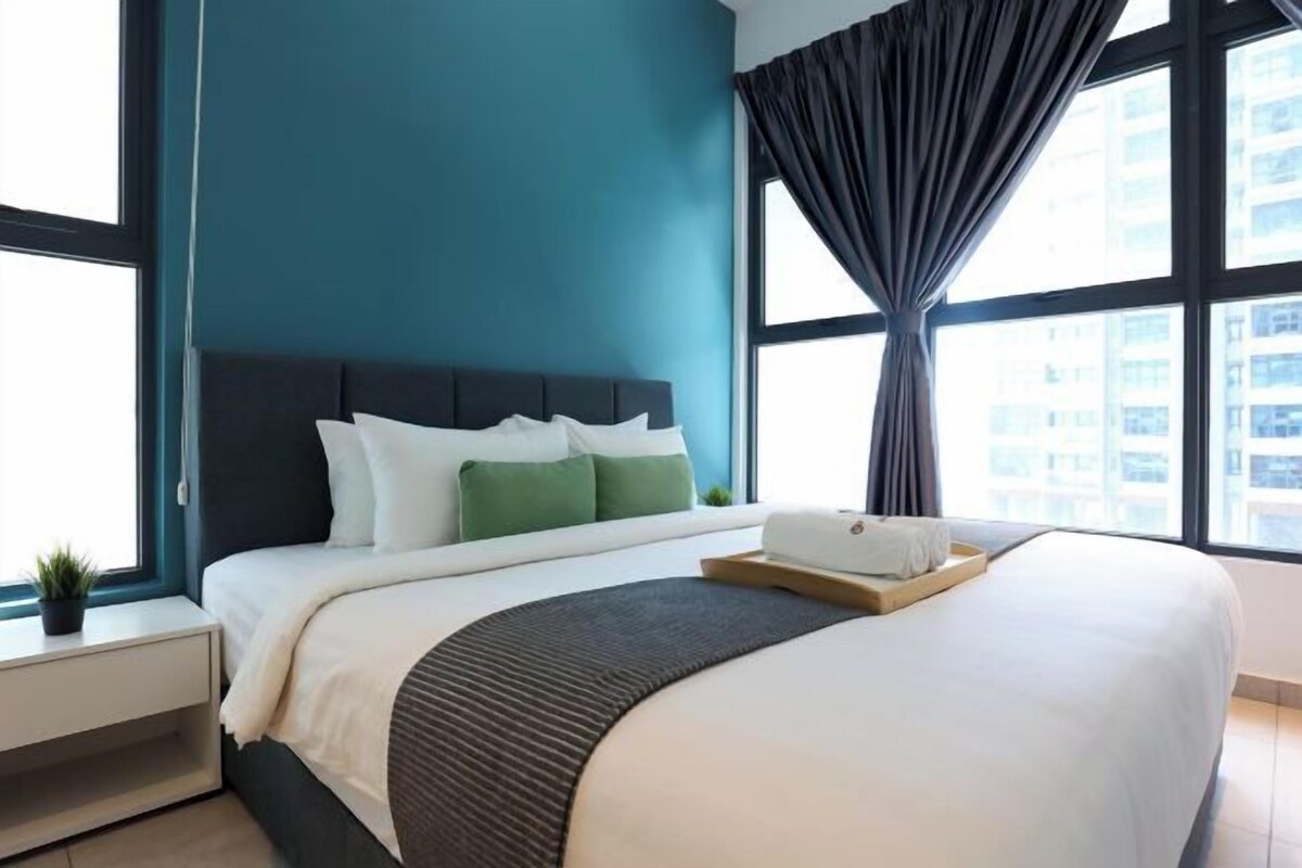 A modern hotel room with a large bed, a bedside table, a window with curtains, and a view of the city.