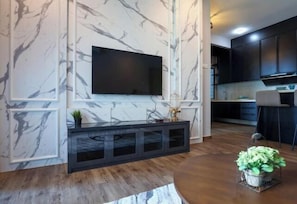Una sala de estar moderna con una pared de mármol, un televisor de pantalla plana, una consola oscura y una mesa de centro redonda con una planta.