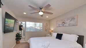 A bedroom with a large bed, a ceiling fan, a TV mounted on the wall, a window with blinds, and a painting on the wall. - Sacramento 4 Bedroom Home | Pool Hot-Tub Mini Golf (Sacramento)