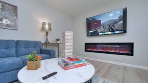 A living room with a blue sofa, a white coffee table, a TV mounted on the wall, and a fireplace. - Sacramento 4 Bedroom Home | Pool Hot-Tub Mini Golf (Sacramento)